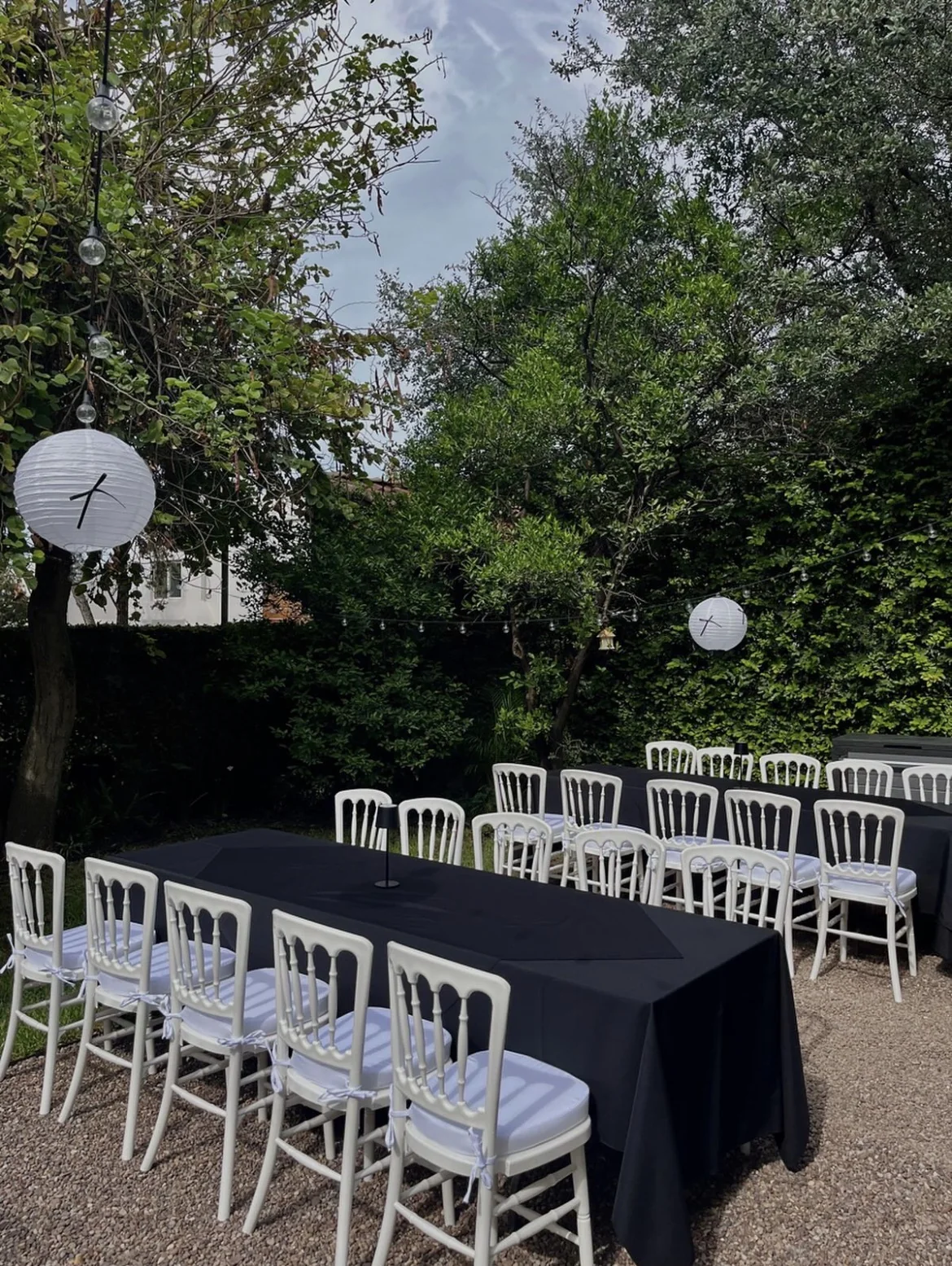 Montaje social con mesas negras y sillas blancas en jardín